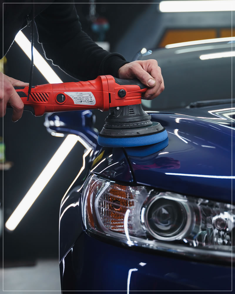 Polimento com politriz na carroceria azul de um carro, próximo ao farol